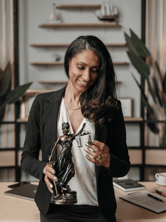 Femme souriante tenant une statue de la justice dans un bureau moderne.