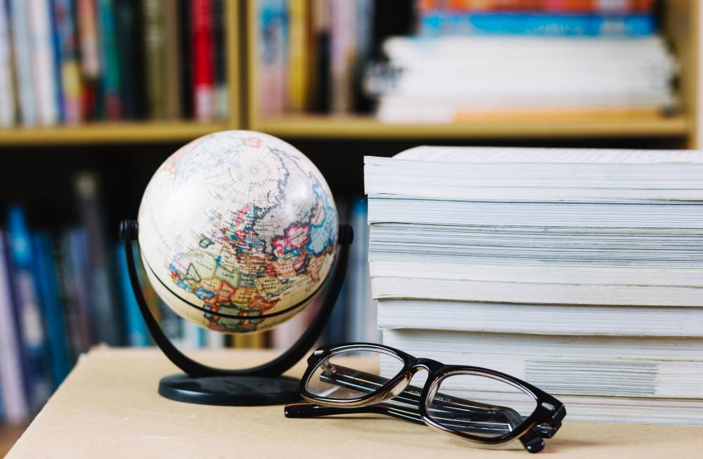 Globe, pile de livres et lunettes devant étagère.